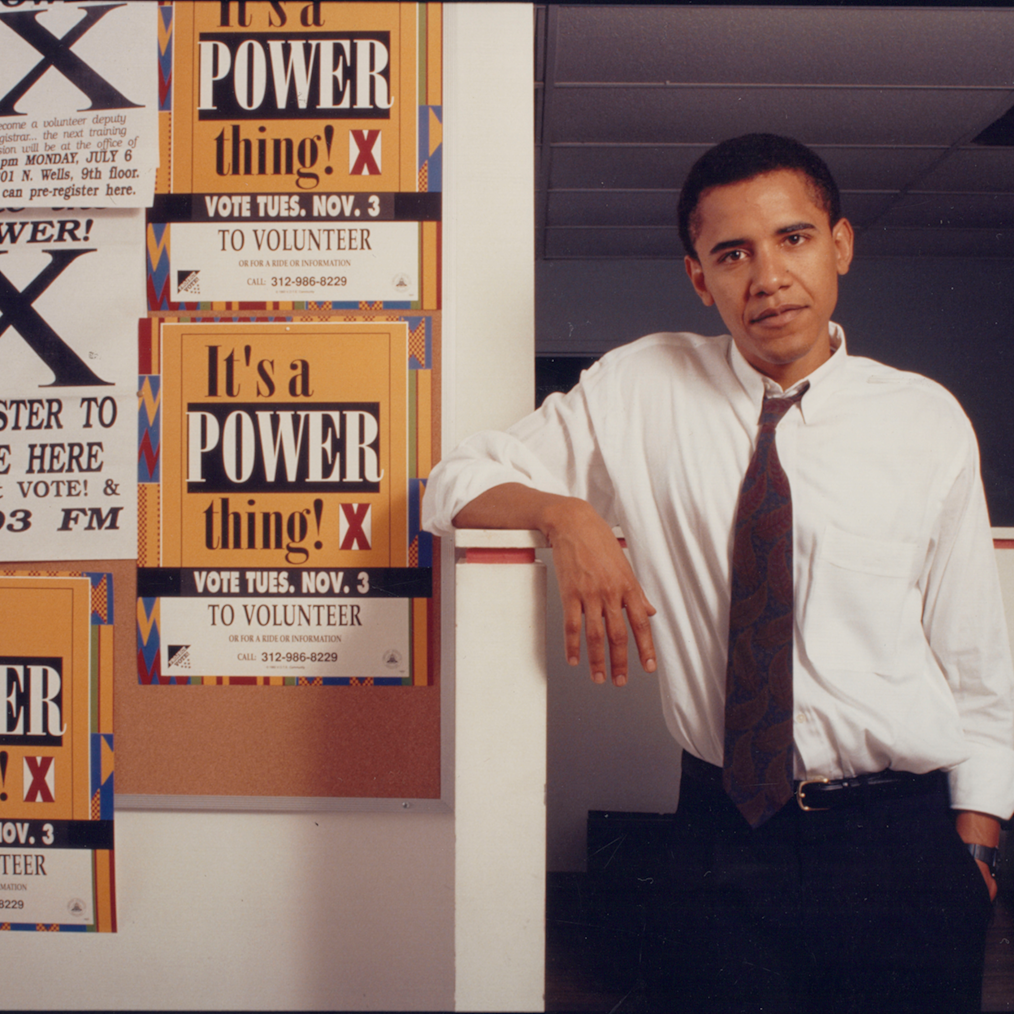 A photo of a young Barack Obama posing beside posters that read, “It’s a Power Thing.” The Building Lives of Service exhibit highlights the early lives, mentors, and community influences of Barack and Michelle Obama.