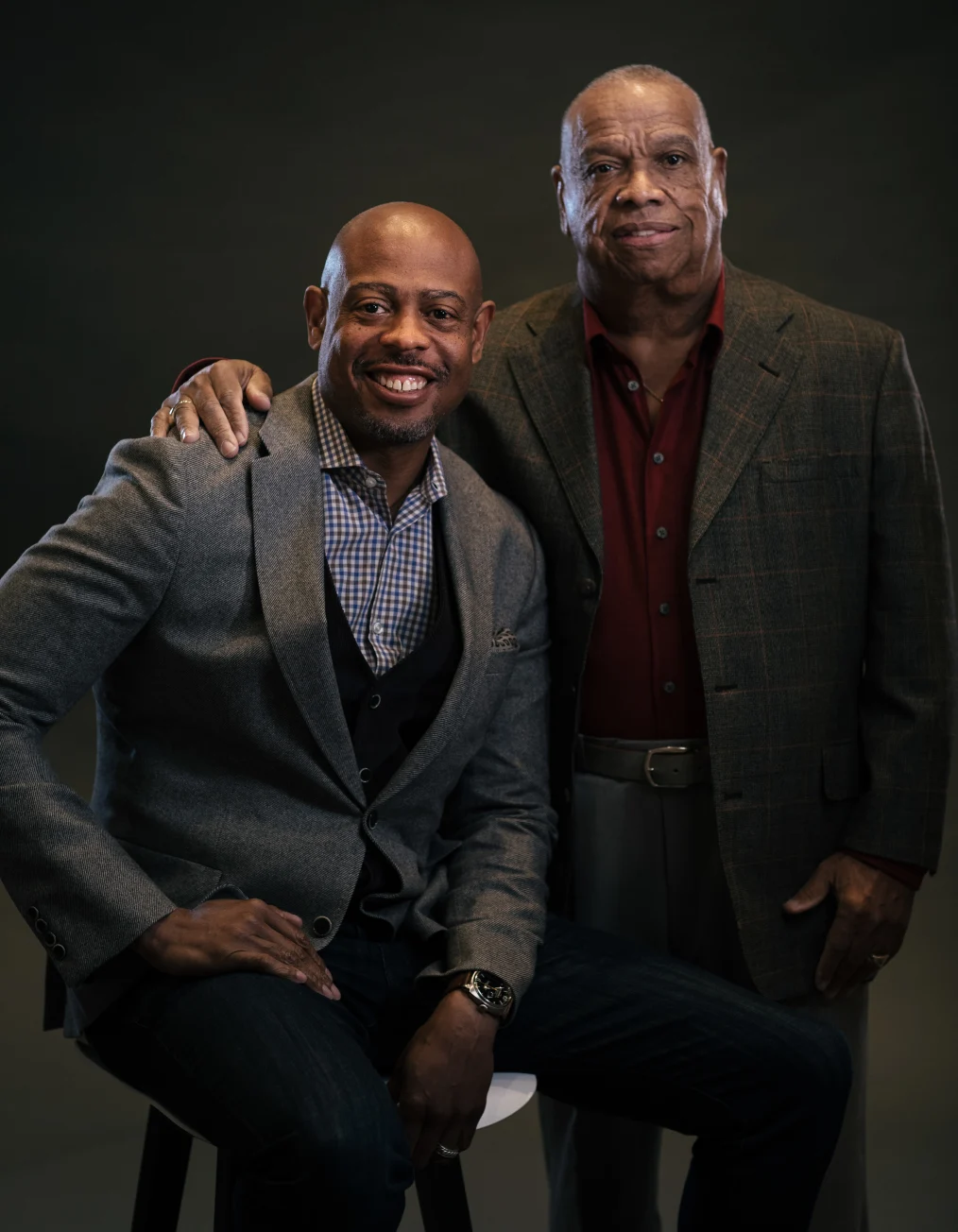 This picture shows two men with deep skin tones wearing business casual clothes smiling toward
the camera.