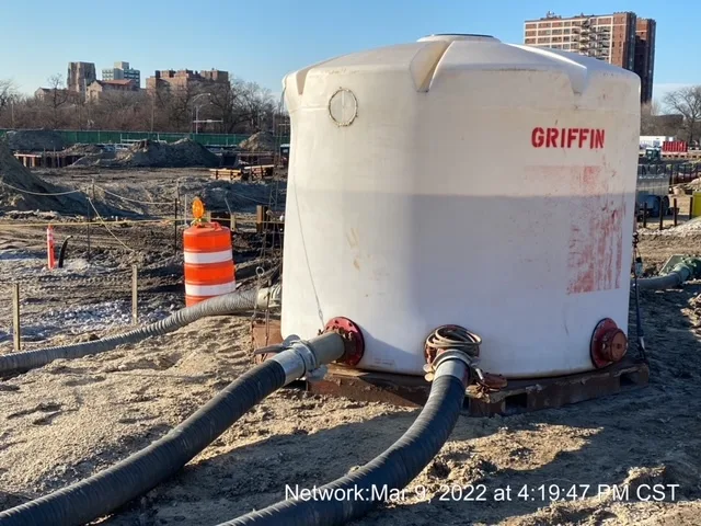 A large, white plastic water container with the words "Griffin" stamped in red. Two flexible pipes run from the bottom.