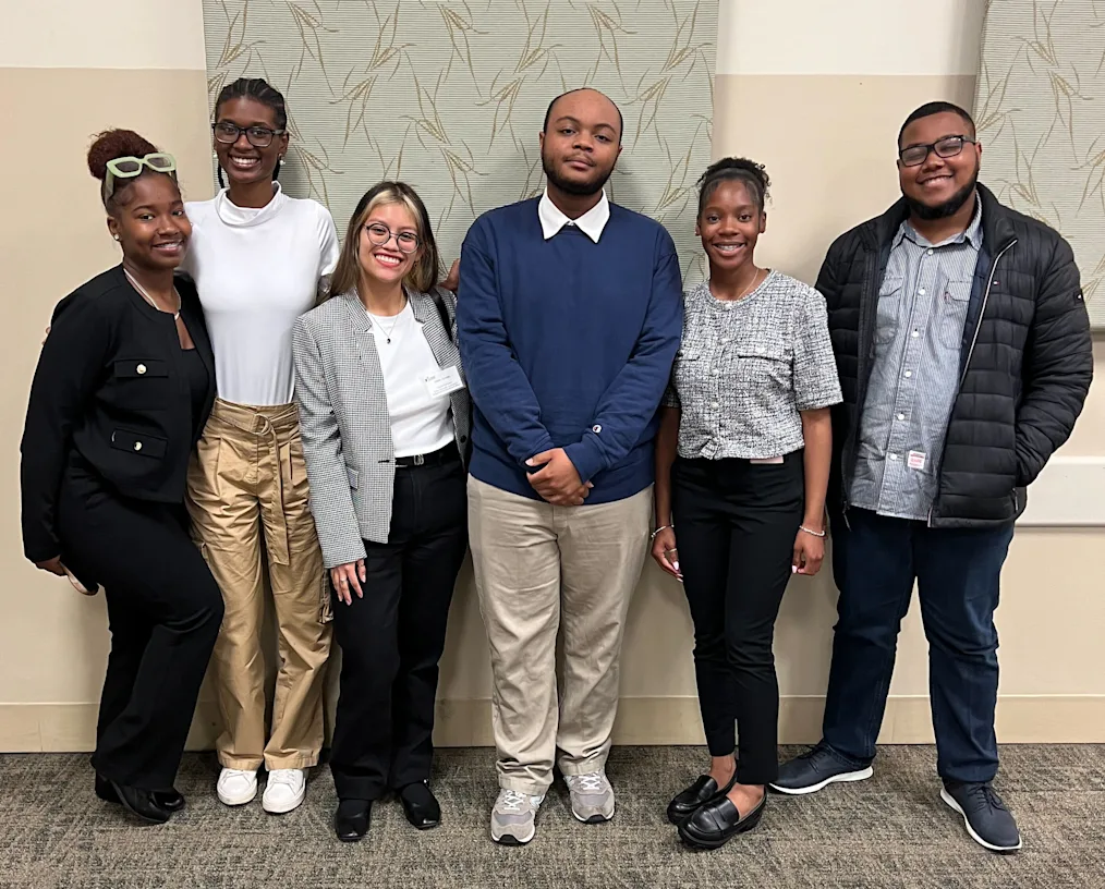 Obama Foundation staff pose with students a part of the Obama Youth Jobs Corps. All are smiling and are a range of light to dark skin tones. 
