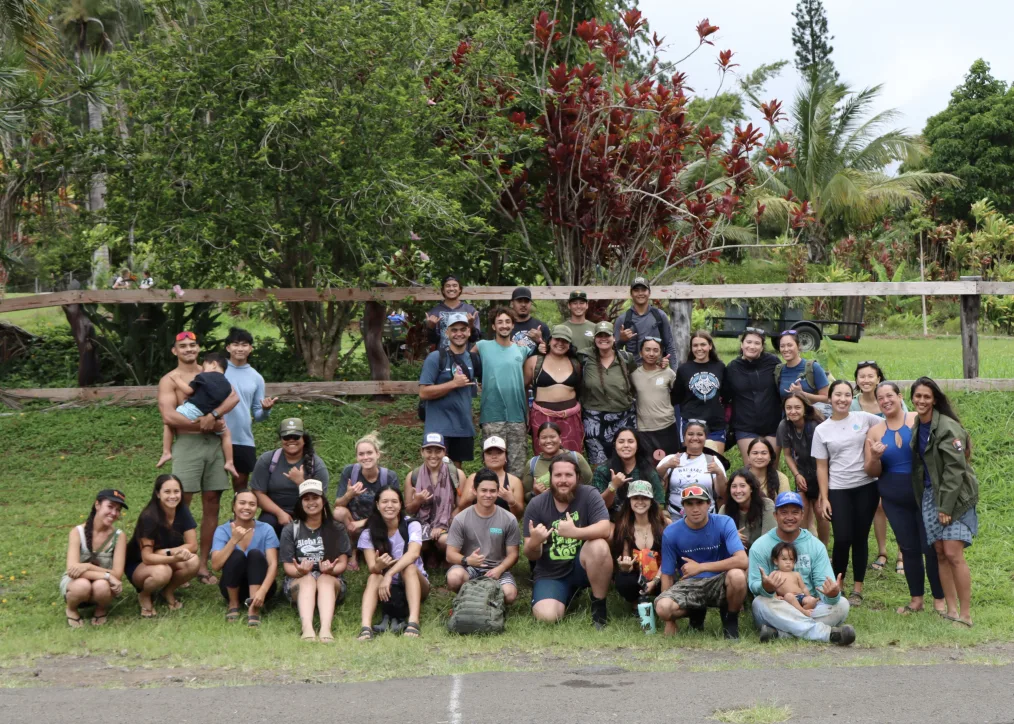 Nalu OʻConnor, a man with a light skin tone and light brown hair, poses in a group photo outdoors with a group of people with a range of ages and light to medium skin tones. All are dressed in workout clothes. 