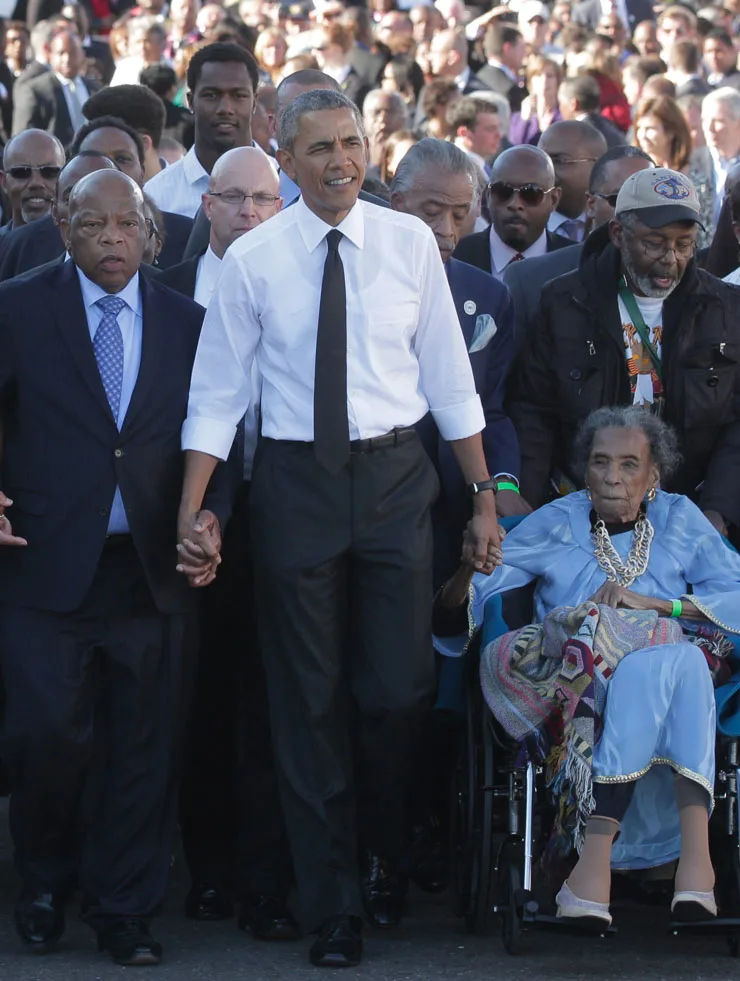President Obama holding hands with people as they all march with many other people behind them