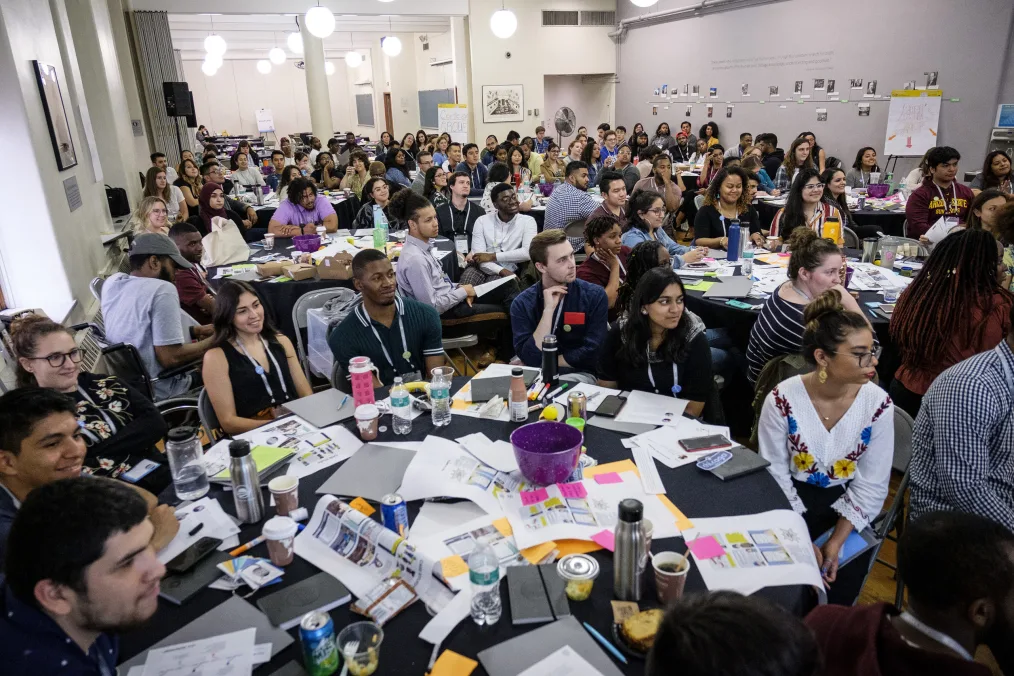 A room filled with 100 young people from all over Chicago sit at cluttered tables.