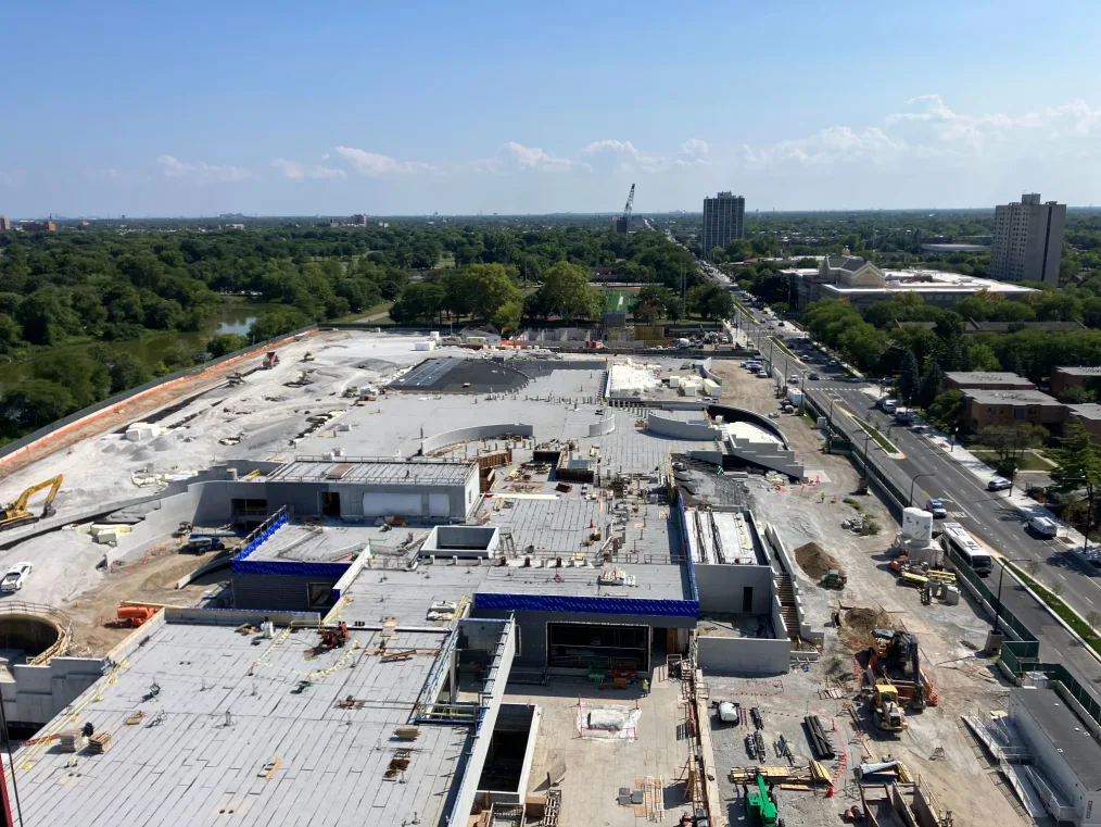 A central and south campus view from Level 7 of the Museum Building at the Obama Presidential Center shows the new elevated green spaces that will span the rooftops of the Forum, Library and parking garage. To the left, geofoam covered by landscaping fabric and gravel forms the base of the landscape that will slope down toward a new walking path and the lagoon.