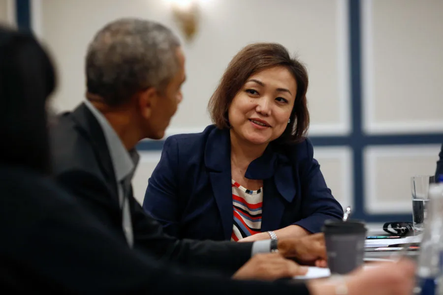 An Asian woman with a light medium skin tone tallks to President Obama. His back is to the camera. She has short brown hair and is wearing a midnight blue blazer. 