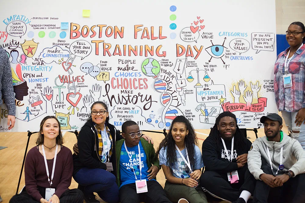 A group of participants pose in front of a board of vidual notes at the Obama Foundation Pilot Training Day in Boston.