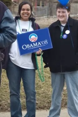 A woman with a medium-deep skin tone holds an Obama foundation sign, while a man with a light
skin tone is holding a blue balloon. Both are smiling toward the camera.
