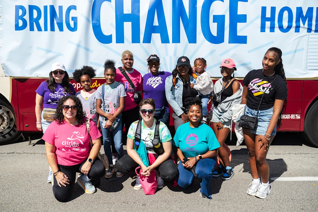 A group of people with a range of light to dark skin tones pose in front of a banner that reads, “Bring Change Home.” 