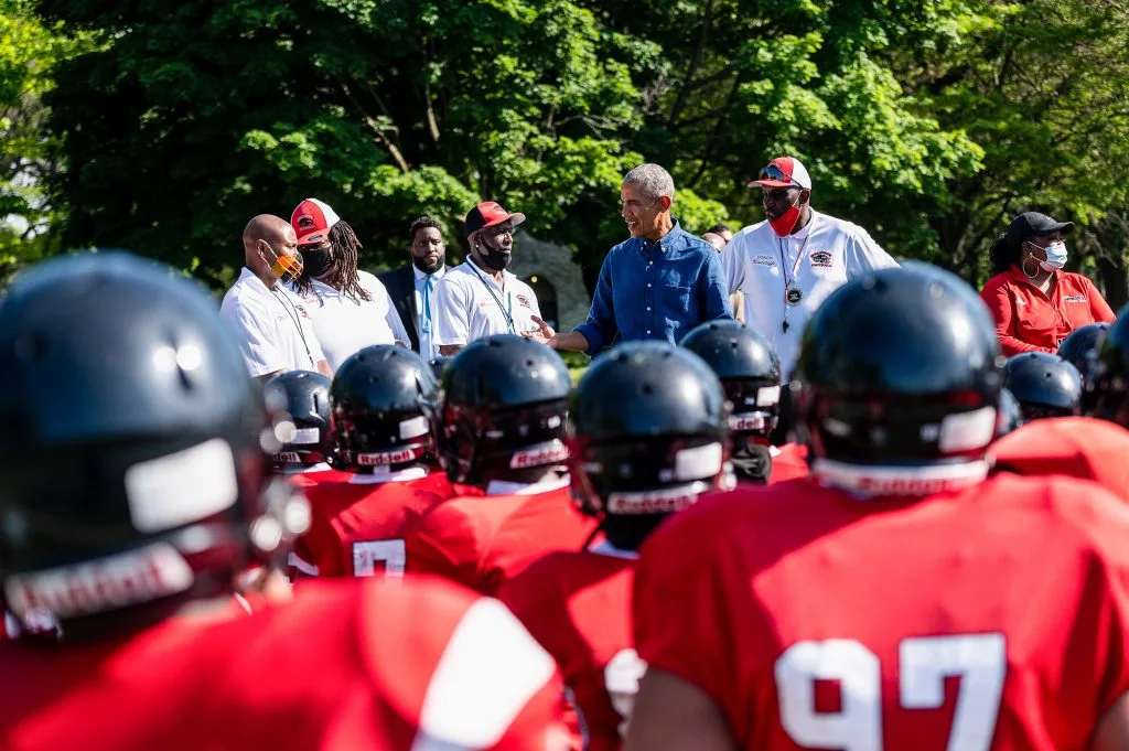 President Obama is seen amongst the backs of football helmet-wearing young people