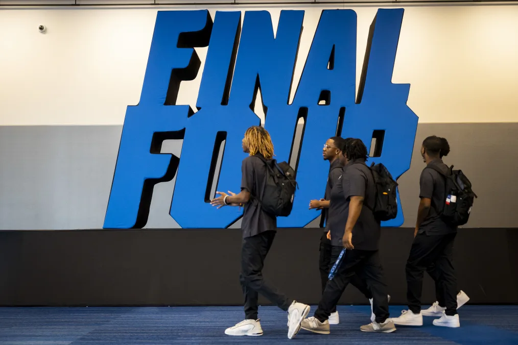 Four young Black men with a range of light to deep skin tones walk past a sign that reads, “Final Four.”