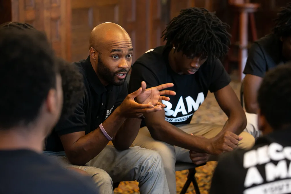 A man gestures to a group of young men sitting in a circle.