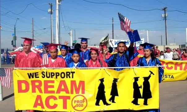 A group of young men and women with a range of light to medium skin tones walk behind a banner that reads, “We support DREAM Act” in Phoenix in May 2007. 