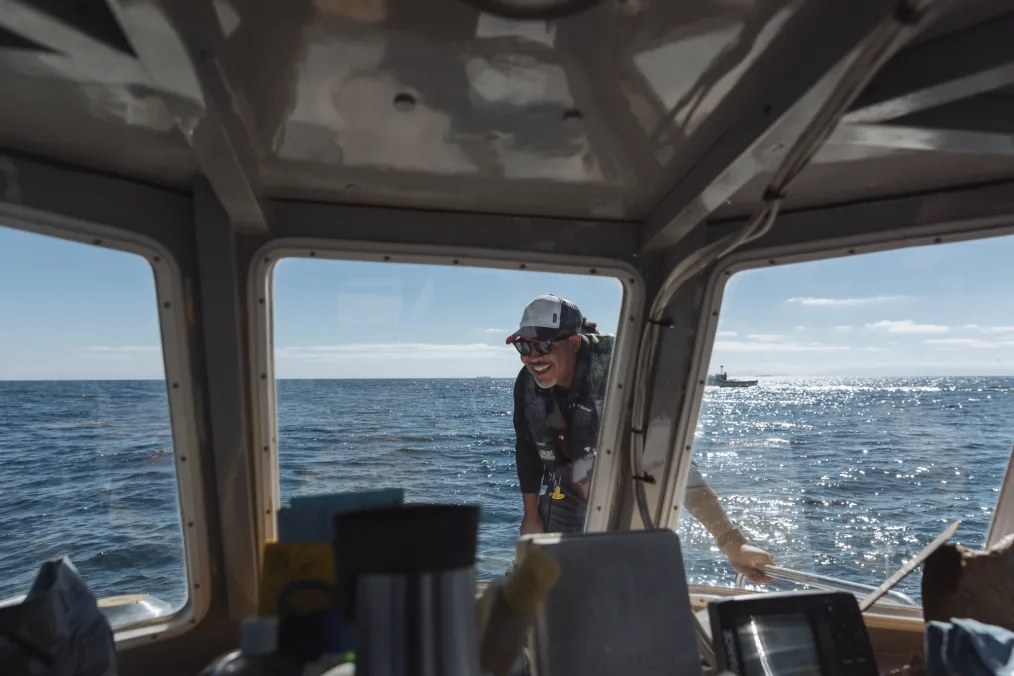 A  man with light skin tones takes a picture on the outside of a boat while out at sea 