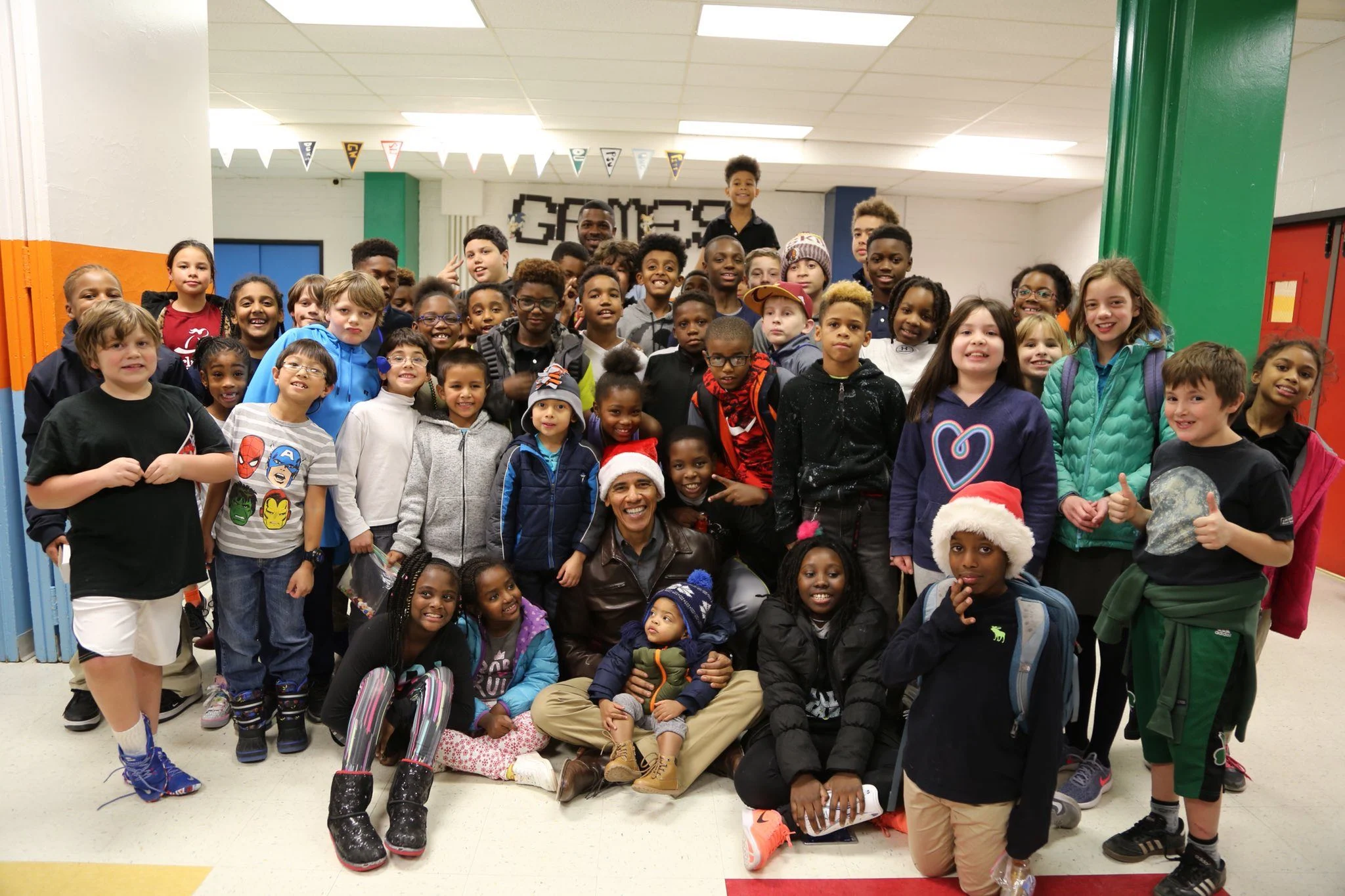 A large group of kids in a elementary school pose for a photo. They are various ethnicities and have a range of light to deep various skin tones.