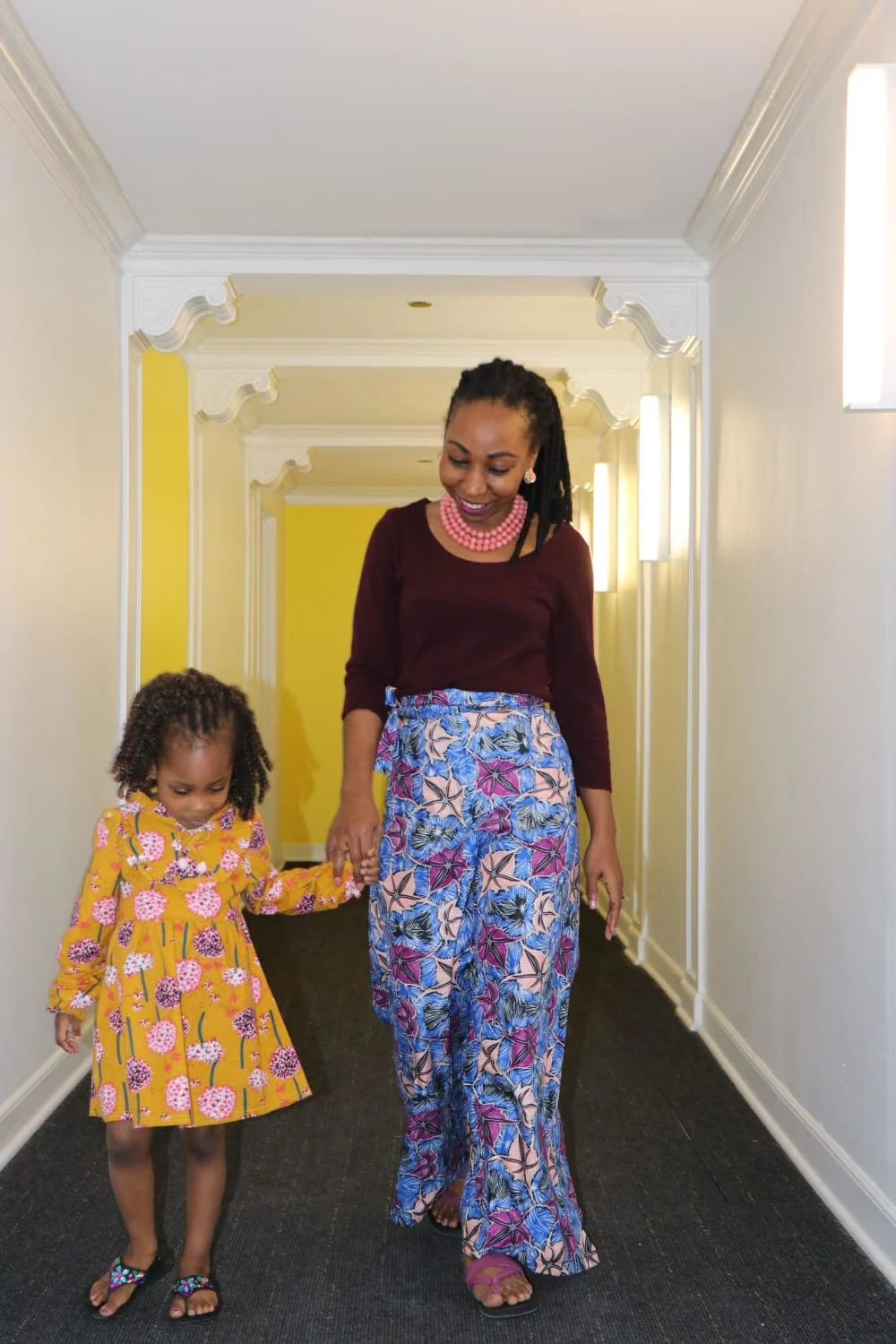A woman and her daughter who are medium brown holding hands while walking wearing floral formal clothing