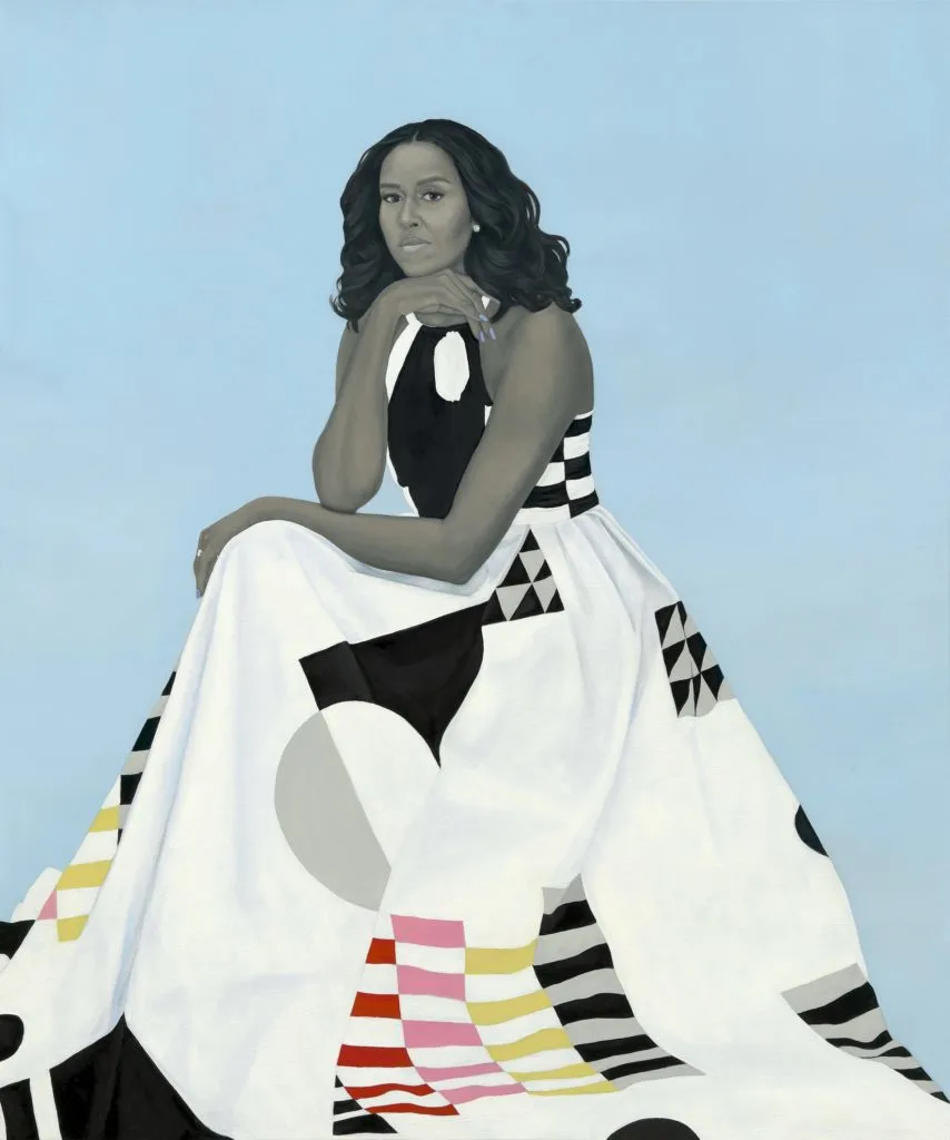 The White House portrait of Former First Lady, Michelle Obama. She is sitting down with shoulder length, black, curly hair, blue nails, and a white dress with black, grey, yellow, pink, and red patterns. The background is light blue. 