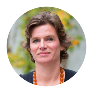 Mariana Mazzucato has a closed-lip smile. She has a light skin tone and short brown hair. She is wearing a blue top and an orange beaded necklace.