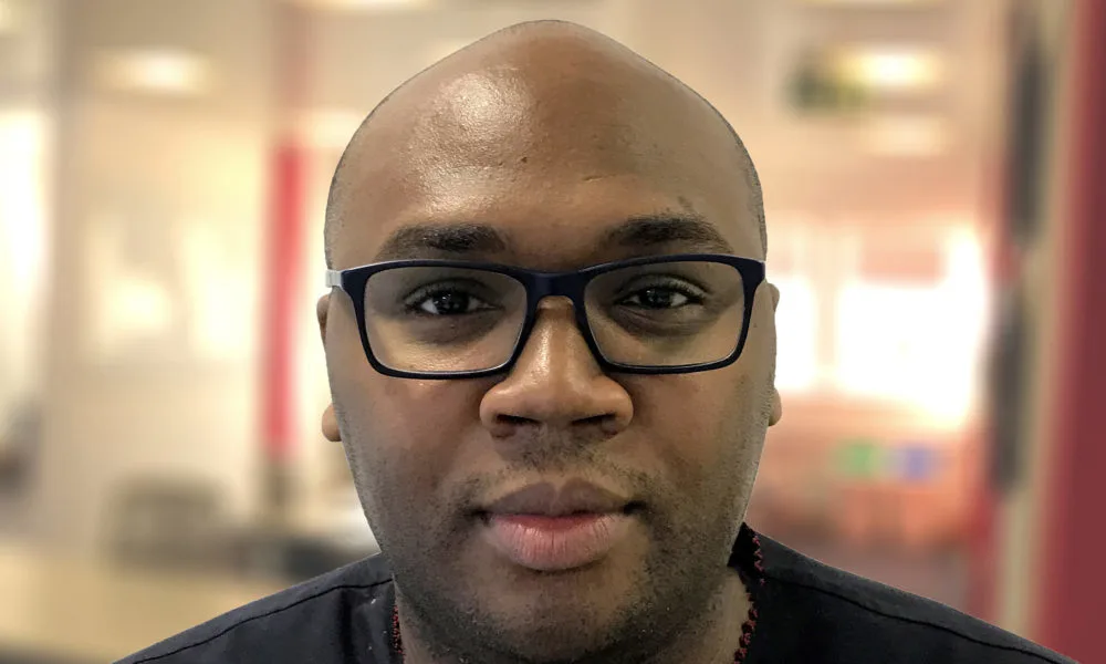 Jason Njoku, a black man with a medium-deep skin tone, shaved head, stubble, and black glasses looks into the camera