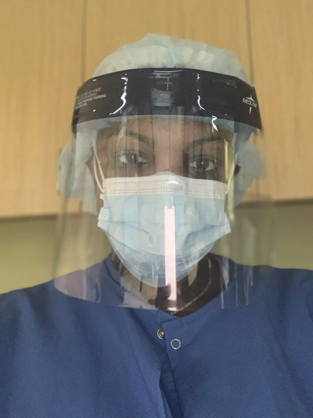 A woman with a dark skin tone takes a selfie in nursing clothing with a mask on