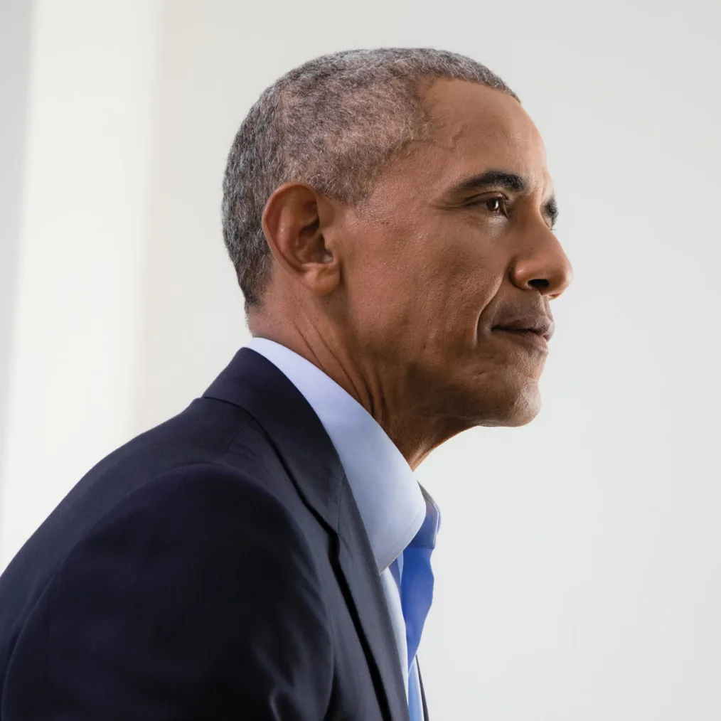 A close-up side portrait of Barack Obama wearing a suit and blue tie. 