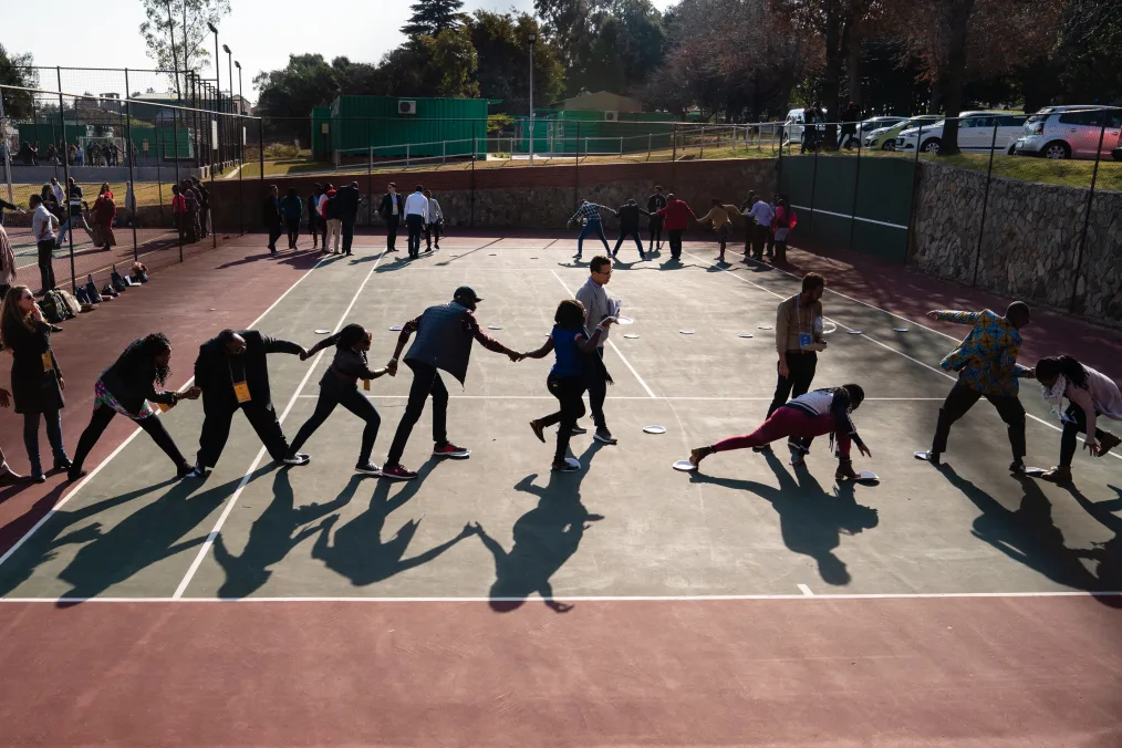A group of children and adults of various skin tones walk holding hands across a basketball court.