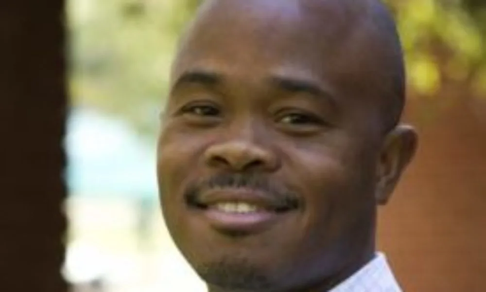 Fred Swaniker, a black man with a medium-deep skin tone and shaved head smiles toward the camera