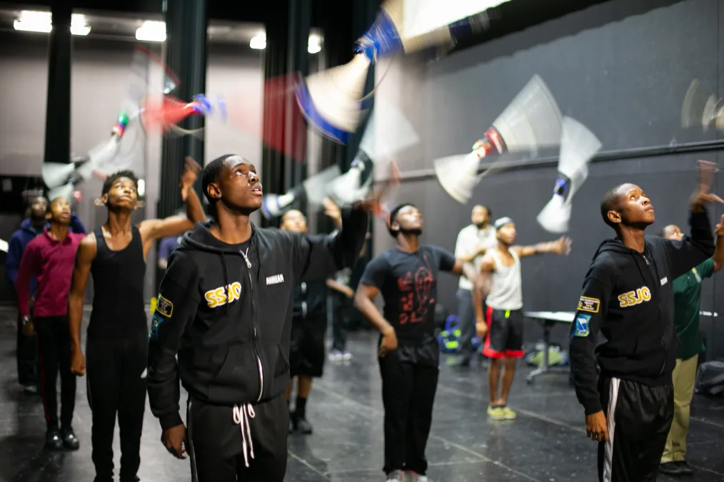 A group of young men practice their drill team routine and toss batons in the air.