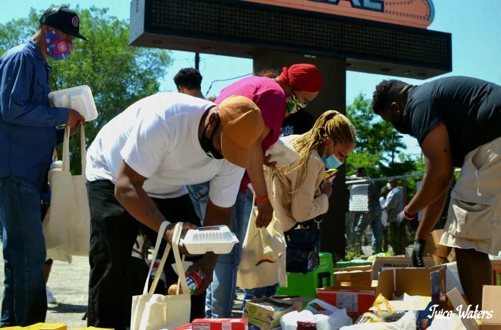 A group of people fill bags with food at an outdoor market.