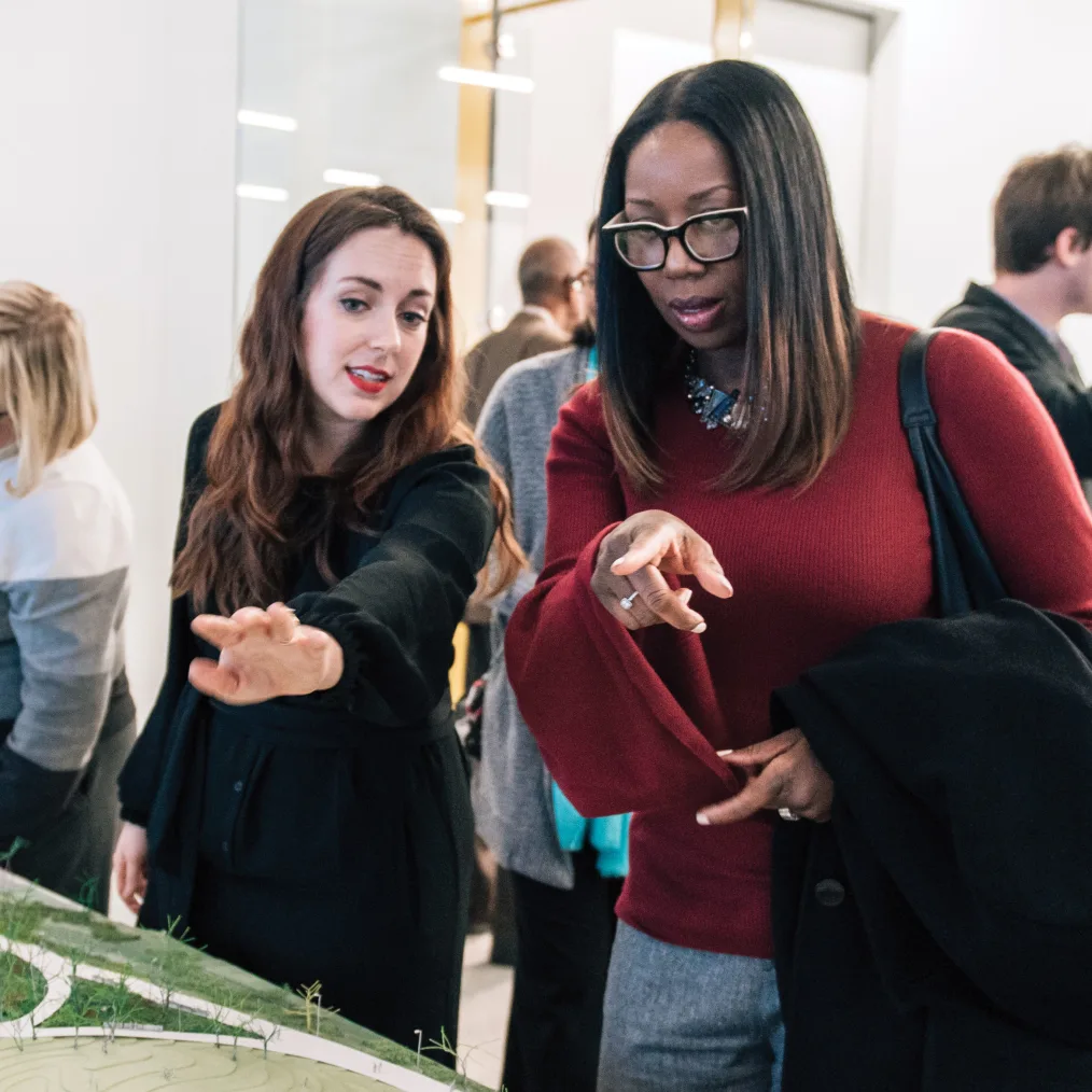 Two women point at the model of the Obama Presidential Center at a public meeting.