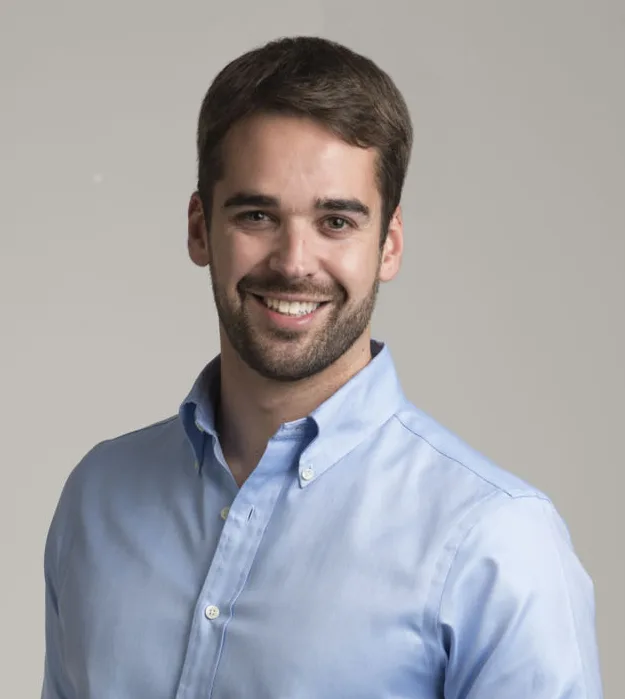 A headshot of a smiling White man with light brown hair and beard. He wears a light blue button-up shirt.