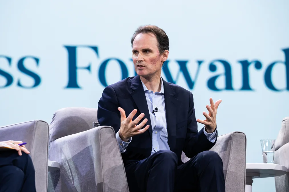 John Palfrey, a man with a light skin tone and thin brown hair sits on a panel at the Obama Foundation Democracy Forum. A sign behind him reads, “press forward.”