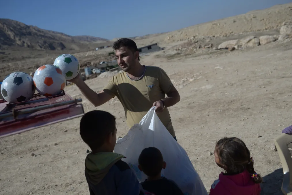 A man holds soccer balls above the heads of small children.