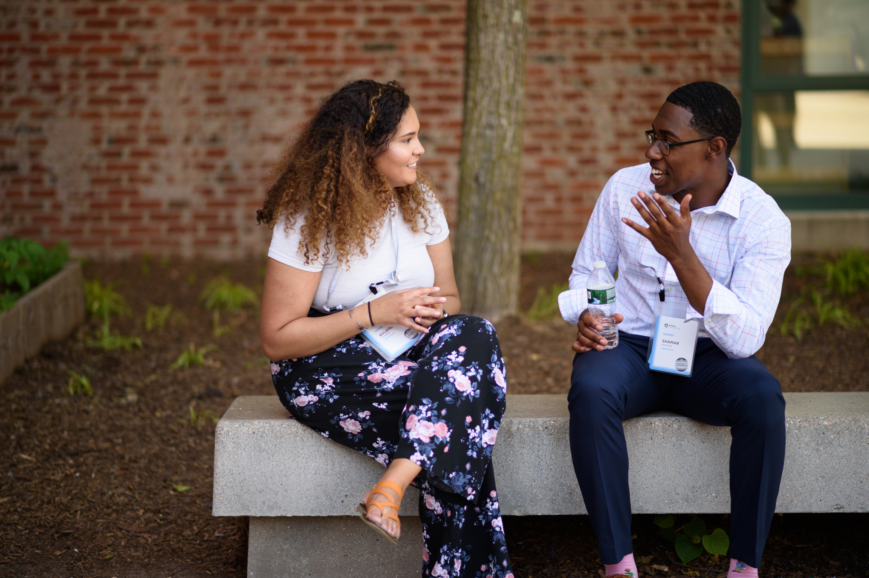 A young man and woman sit in conversation on a park bench.