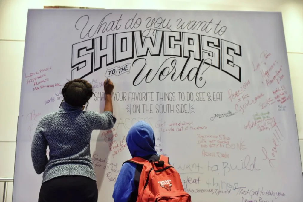 An adult and child write on a large paper with the text "What do you want to SHOWCASE TO THE world?" in various styles of fonts.
