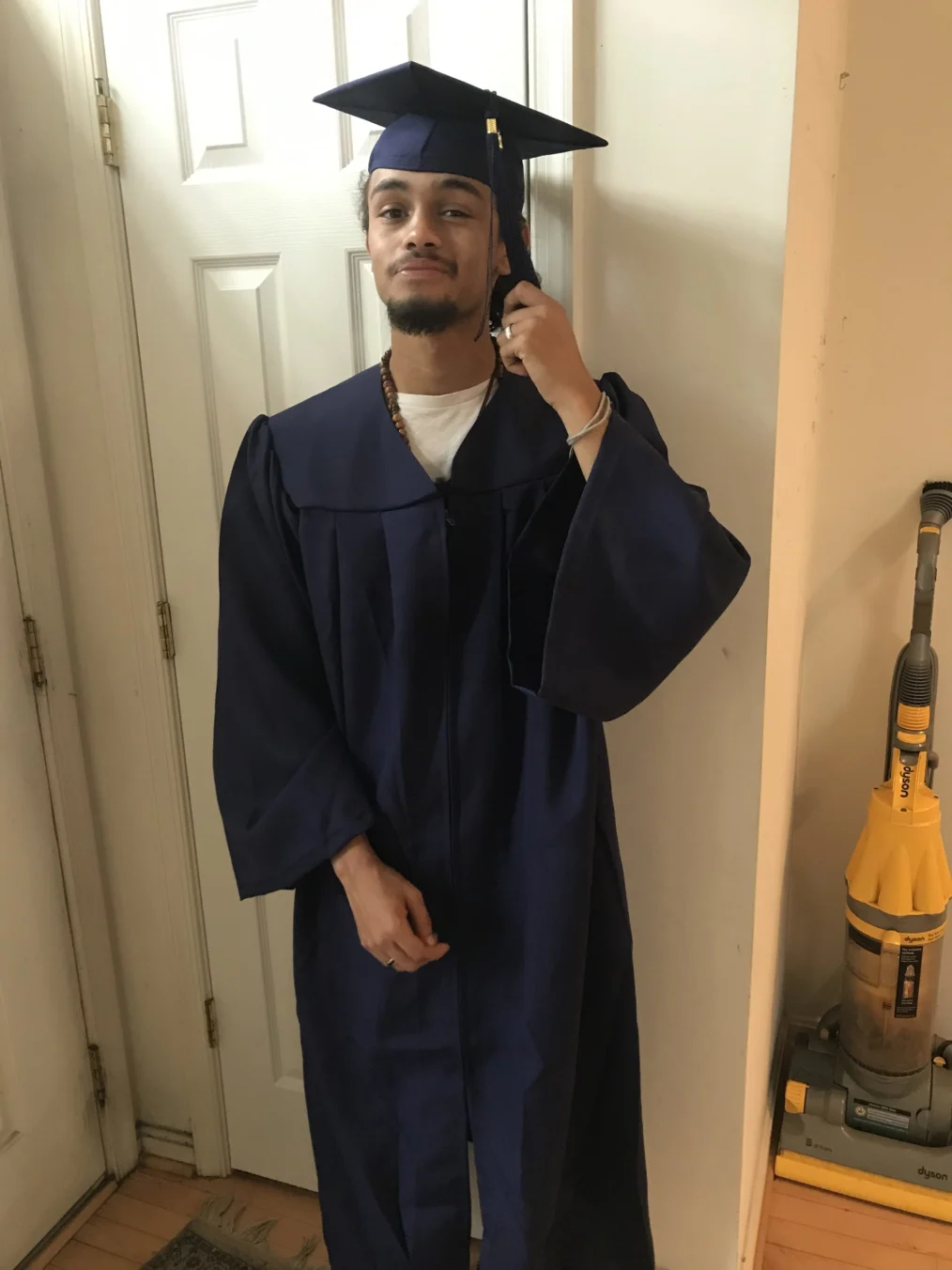 A male with a light-medium skin tone takes a picture in hs cap and gown