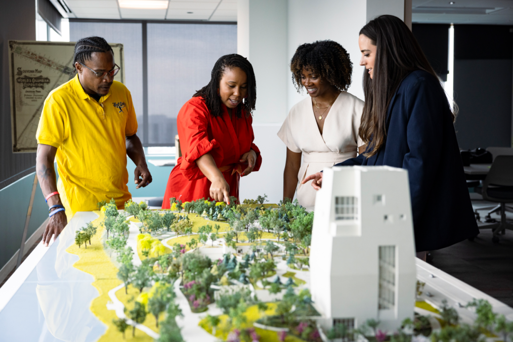 An image of four people with a range of light to dark skin tones, reviewing and looking at the 3D model of the Obama Presidential Center.