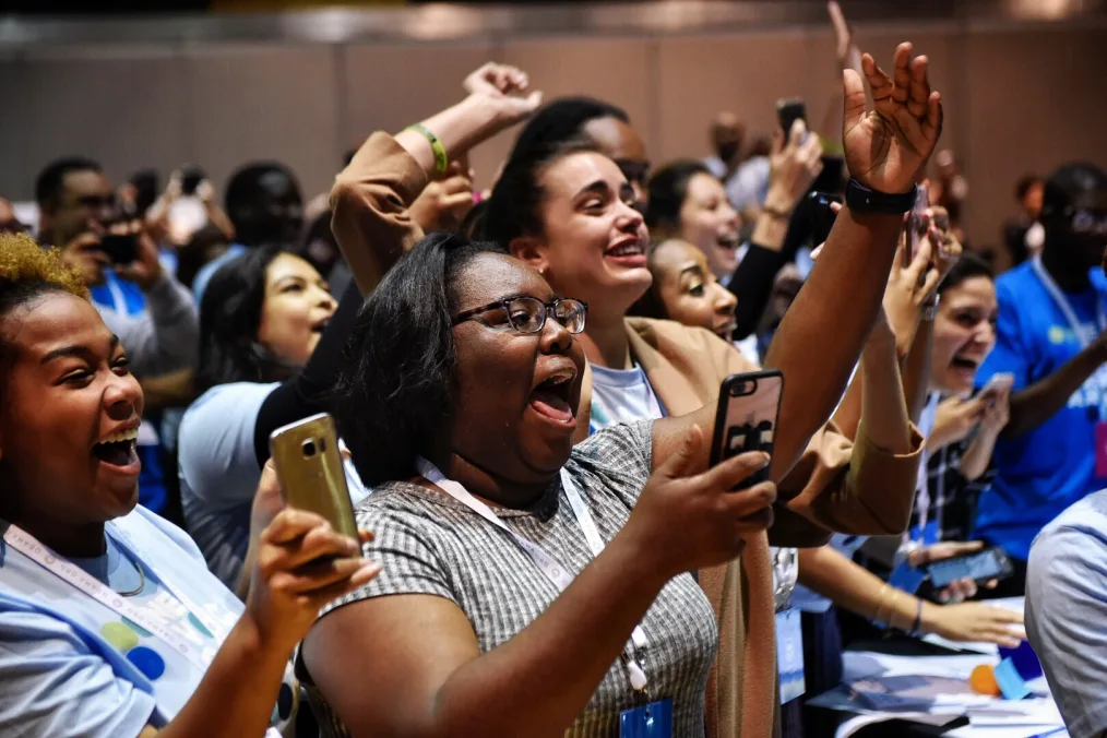 A diverse group of people screaming and holding their phones up 