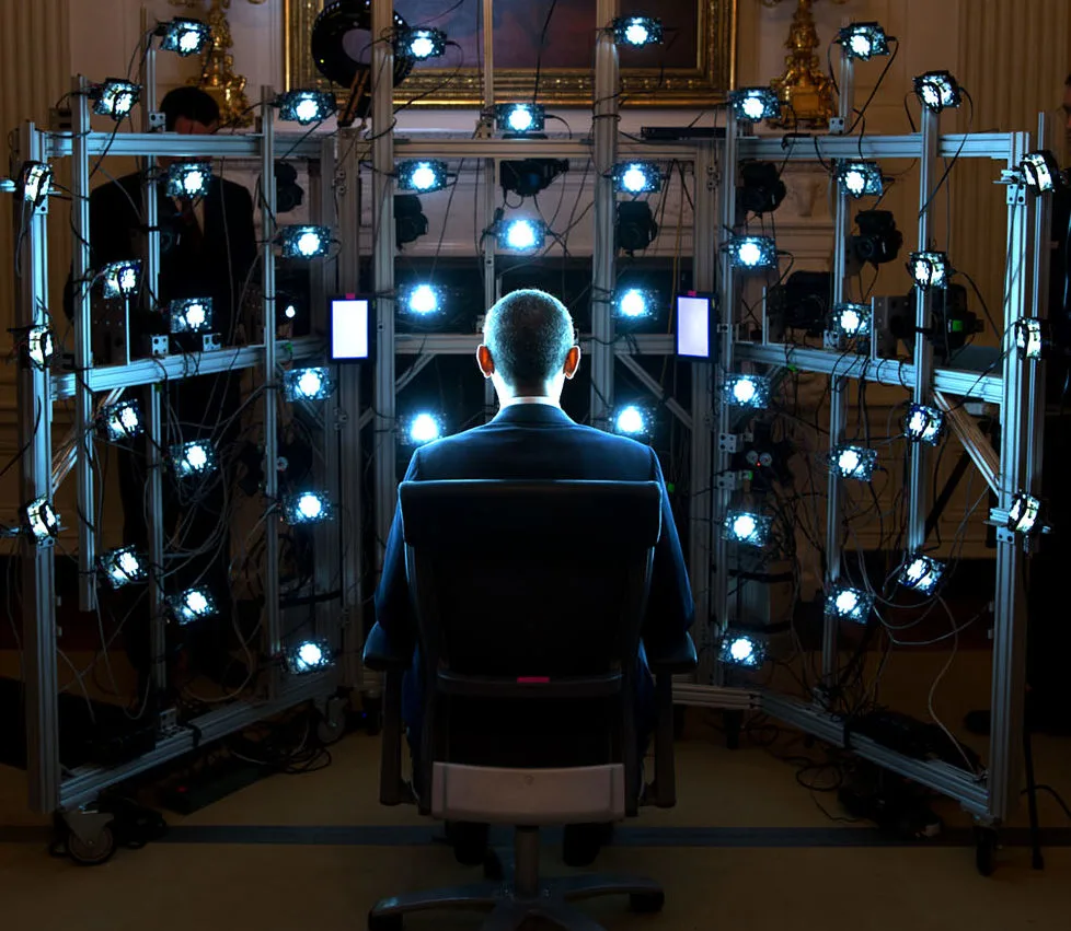 A man sits in a chair while dozens of bright lights surround him on a grid framework.