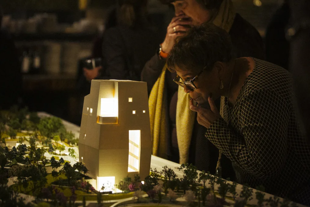 Two women peer into the lit windows of the Obama Presidential Center model.