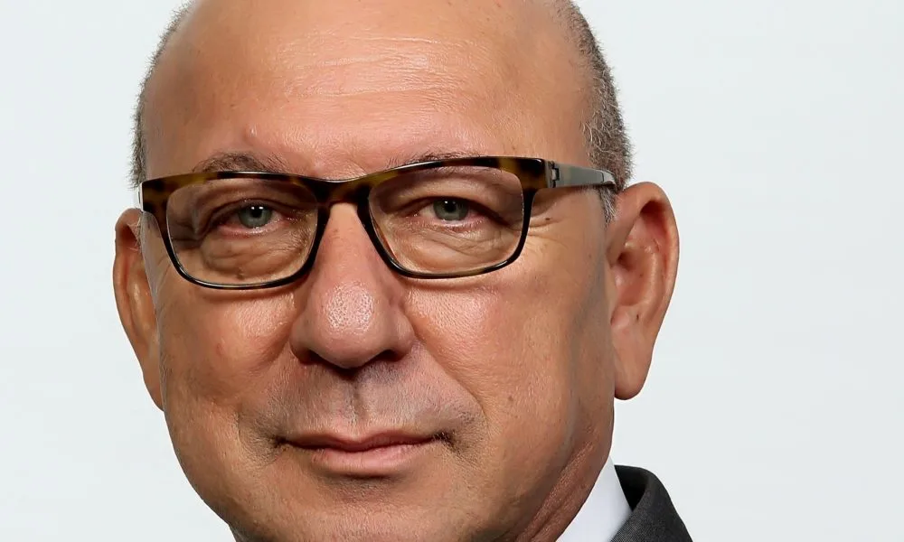 Trevor Manuel, a man with a light skin tone, shaved head, and glasses looks into the camera.