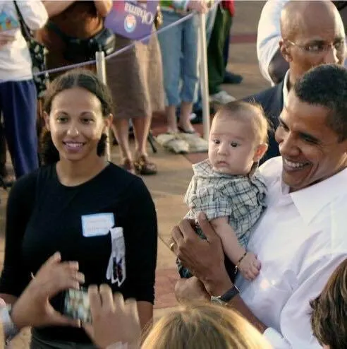In this picture, President Obama is holding a baby with a light skin tone while posing for a picture.