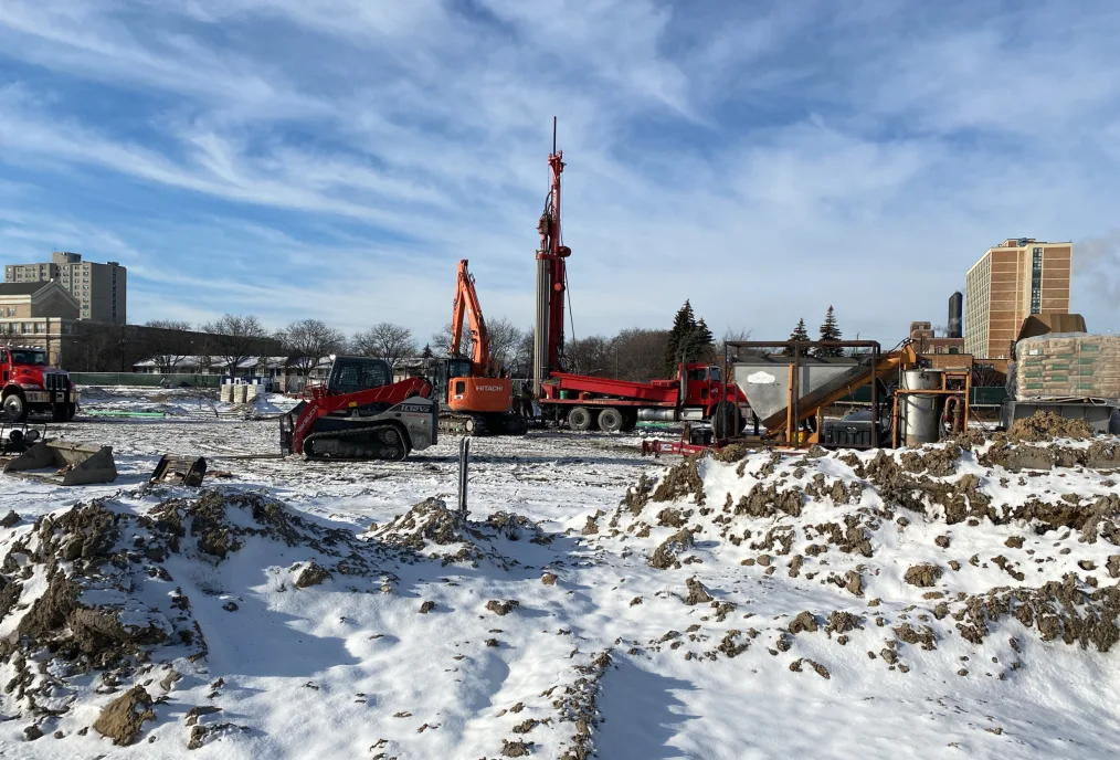 A snowy, muddy construction site with the rectangular outline of metal and red pipe.