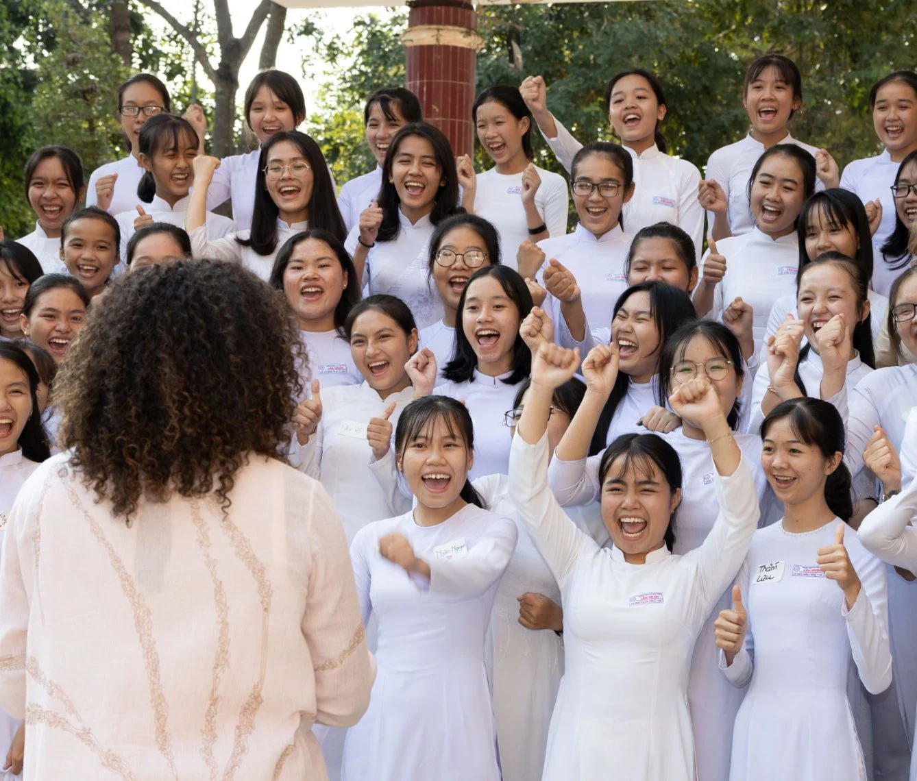 Mrs. Obama faces a group of excited young girls wearing white robes with their hands above their heads in joy.