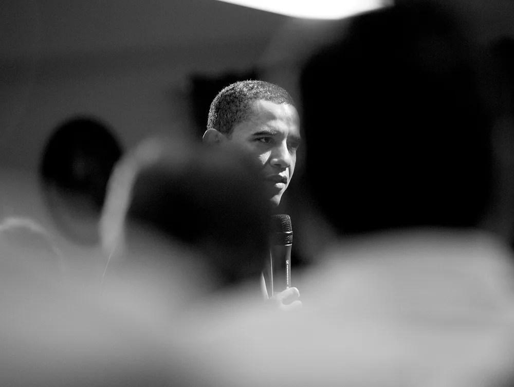 A black-and-white  photo of Barack Obama as seen through out-of-focus heads in the foreground.