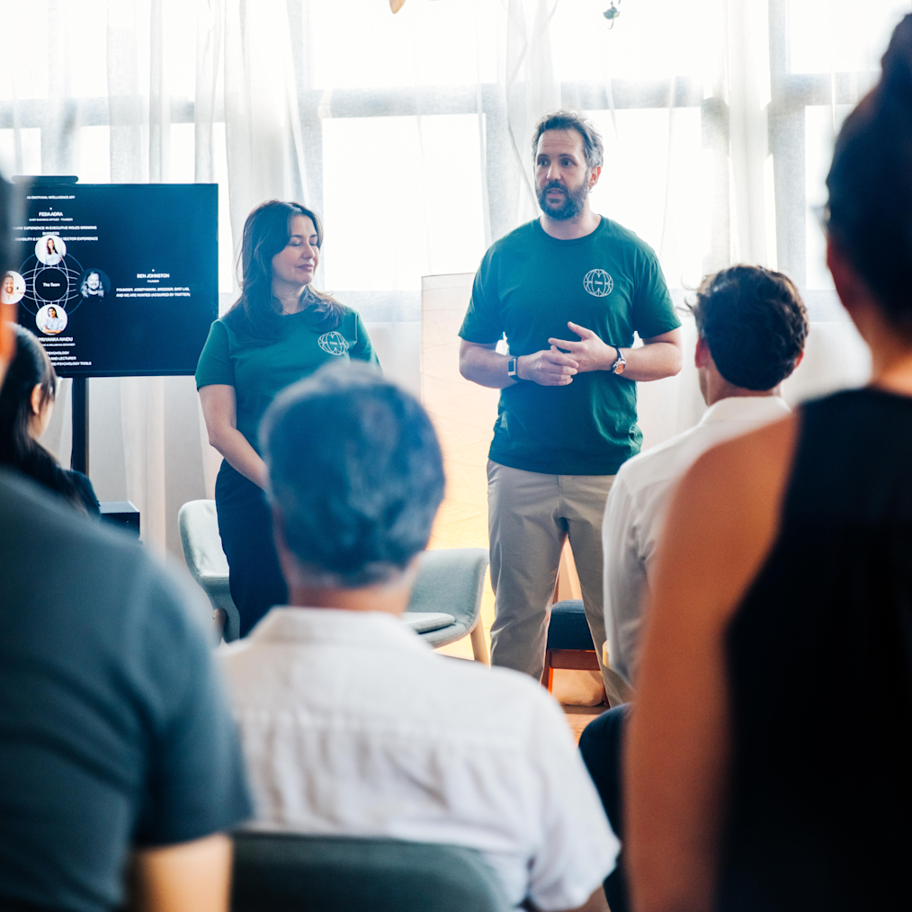 William Stubbs, a man with a light skin tone, stands on the right of Feda Adra, a woman with a light skin tone, cofounder of Dala, at a Dala event. Both are wearing tshirts and have dark hair.
