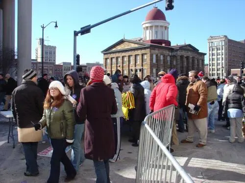 A crowd of people in winter clothing stand in front of the Illinois state capitol. 