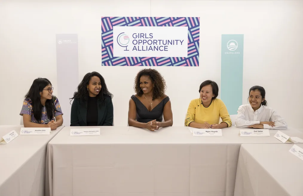 Mrs Obama smiles at a table surrounded by four young women.