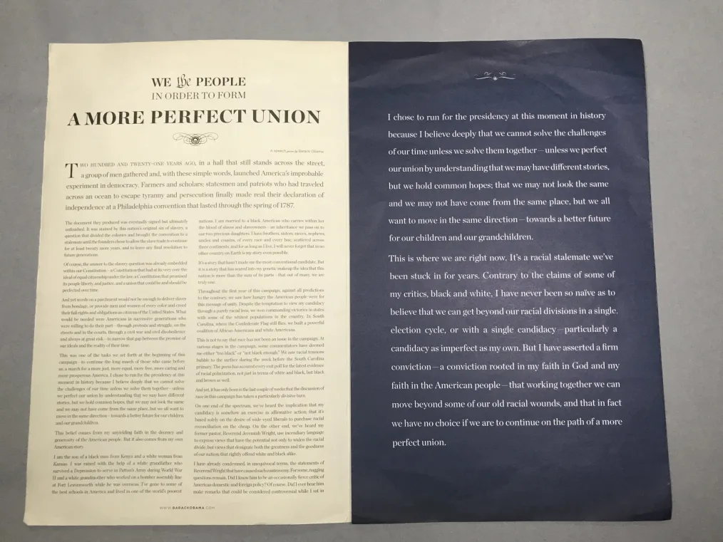 A piece of paper with one half tan-colored and the other dark blue. The words "We the People in Order to Form A More Perfect Union" are at the top of one side, while the other has what appears to be a speech printed on it from the perspective of Barack Obama.