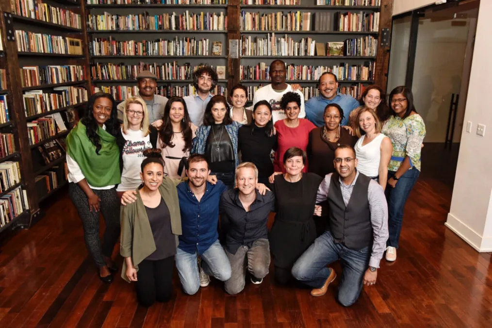 This image shows many people with various skin tones inside a library room posing and smiling
toward the camera.
