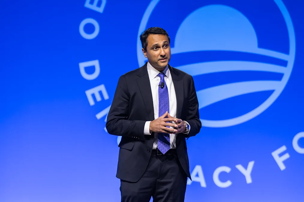 Eboo Patel, a man with a medium skin tone, speaks to an audience. A sign in the background reads, “Obama Foundation Democracy Forum.” 